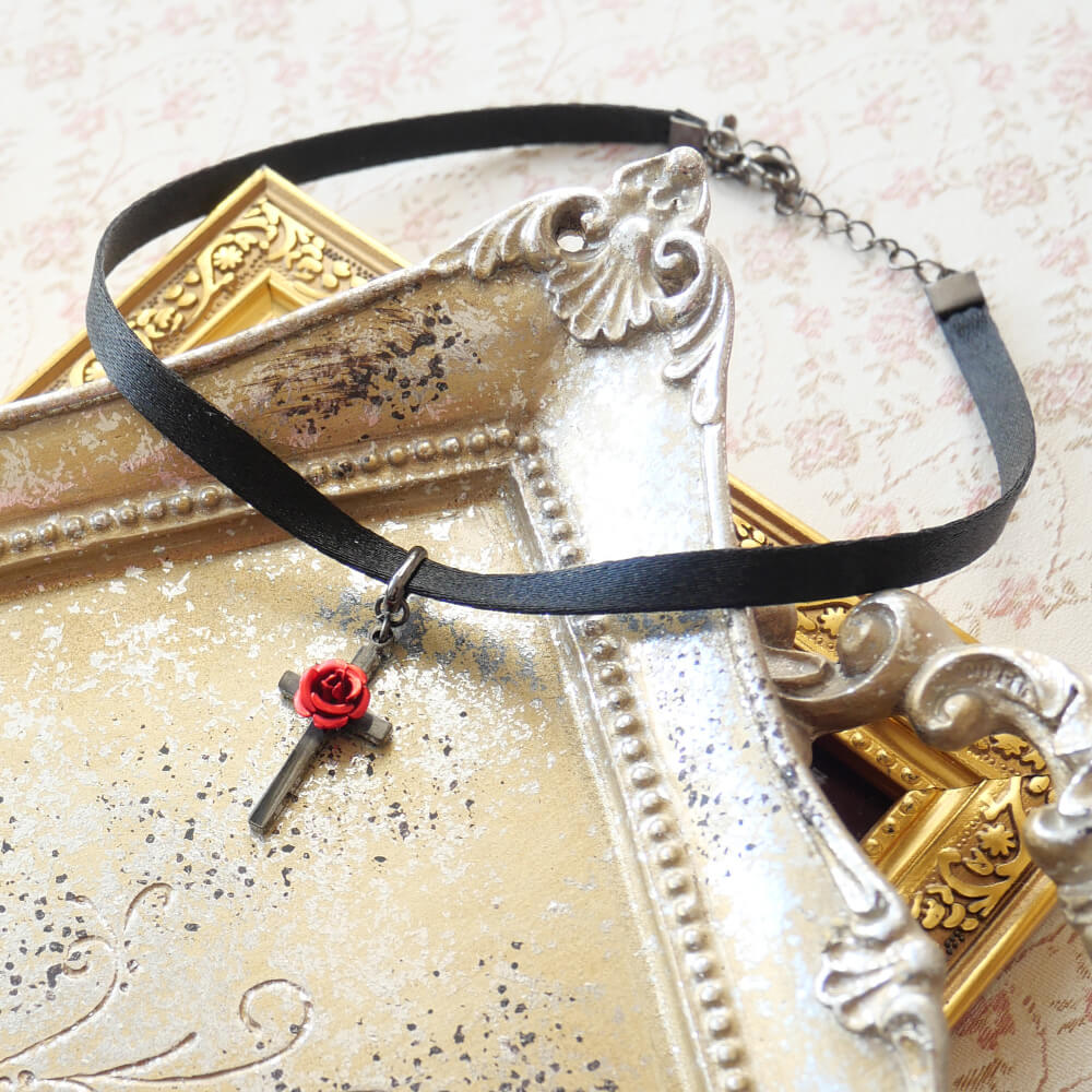 薔薇と十字架が融合したゴシックテイストのチョーカーは、シンプルでありながら首回りを華やかに演出します。 MOKUBA社の高品質なサテンリボンを使用し、肌触りが良く、長時間の着用でも快適です。 ガンメタクロスに薔薇のモチーフをあしらい、シンプ...