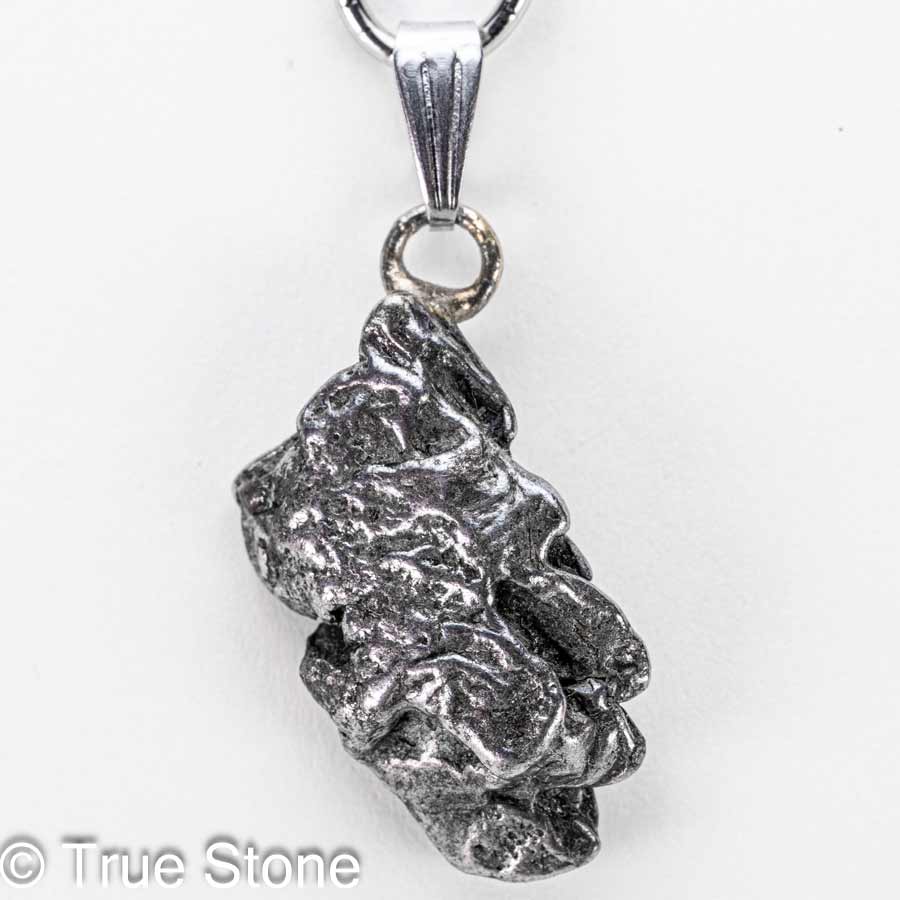 小さな頃、願い事を叶えたい一心で夜空を見上げ「流れ星」を探していたあの日。 不思議と「探す」と見つかりません。 偶然「流れ星」を発見しても、「あっ」と思った瞬間燃え尽きていたあの日。 そういう時に限って「願い事」は忘れています。 それなら、隕石（流れ星）を実際に手に入れて願ってみてはいかがでしょうか。 昔なら「流れ星」を手に入れる事こそが「願い事」だったのかもしれません。 そんな子供の頃の夢や希望が内包する「流れ星」を両手で握りしめると、「当時の自分」を垣間見る事ができるかもしれません。 カンポ・デル・シエロ隕石は、アルゼンチン北部のチャコ州からサンティアゴ・デル・エステーロ州にかけて広がる巨大な隕石散在域で見つかる鉄隕石で、名前はスペイン語で「天の野原（天空の野）」を意味します。 この地帯には数千年前に大規模な隕石の落下が起きたと考えられており、地表には大小のクレーターが点在し、その周囲から無数の破片が採集されてきました。 先住民の伝承や16世紀以降の記録にも「鉄の塊」の存在が語られており、近代的な地質調査によって、広範囲に散らばった鉄隕石群であることが確かめられています。 分類上はIABグループに属する鉄隕石で、主成分は鉄とニッケルの合金です。 ニッケルはおよそ6〜7％前後を含み、これに硫化鉄（トロイライト）、リン化物（シュライバーサイト）、炭化物（コーエン石）などの包有物が散点するため、切断面や破断面に複雑で味わい深い表情を与えます。 内部組織は「オクタヘドライト（八面体構造）」で、適切に研磨・酸エッチングされたスライスでは、カマサイトとテーナイトが幾何学的に組み合わさった有名なウィドマンシュテッテン構造が現れます。 この幾何学模様は、地球上では自然条件下で再現できない極めて遅い冷却過程（数千万〜数億年スケール）でのみ形成されるため、カンポ・デル・シエロをはじめとする鉄隕石の「宇宙由来」の証拠として珍重されています。 大きな個体（ナチュラル・ピース）の外観は、表面に親指で押し込んだような「レグマグリプツ（拇指状凹）」が刻まれていることが多く、これは大気圏突入時の高温・高圧下で溶融と剥離が繰り返された痕跡と解釈されます。 流線痕や溶融皮殻が部分的に残る標本もあり、手のひらサイズでも密度が高く、見た目以上の重量感があるため初見の方は必ずといっていいほど「想像より重い」と驚かれます。 市場では二つの形態が流通します。 ひとつは自然形状を保った個体で、レグマグリプツや溶融痕、自然酸化の風合いをそのまま楽しむコレクション向けのタイプです。 もうひとつは小さなカンポデルシエロをそのままの状態でペンダント等へ利用するジュエリー素材として高い人気を誇ります。 カンポ・デル・シエロは屋外で長期間にわたり風化してきた経緯から、塩化物に起因する錆「隕石病」が進行しやすい個体もあります。 コレクションやジュエリーとして長く楽しむためには、湿気と塩分を避け、素手で触れた後は柔らかい布で油分と汗を拭き取り、乾燥剤を入れた密閉容器で保管するのが基本ですがカメラ用防湿庫があれば最適です。 ※当店では隕石に錆止めスプレーを施し、カメラ用防湿庫に湿度10％〜20％で保存しています。 パワーストーンの観点では、カンポ・デル・シエロは「地球外の鉄（宇宙鉄）」としてグラウンディングと意志力の強化、行動力の点火を象徴すると語られることがあります。 科学的効能を保証するものではありませんが、何十億年の時間を経てきた物質を手にする体験は、創作や決断の背中を押す“物語性の力”をもたらしてくれるでしょう。 総じて、カンポ・デル・シエロ隕石は、学術的にも審美的にも「鉄隕石の醍醐味」を一本で味わえるオールラウンダーです。 自然のレグマグリプツを残した個体は荒々しい宇宙の息遣いを、エッチングしたスライスは宇宙時間の結晶学を、それぞれ手のひらサイズで見せてくれます。 本品は研磨や酸処理を一切施していない、自然なままの隕石です。 鉄隕石は本来、黒みを帯びた風合いを持ちます。 市場では金属光沢を強調するために表面を研磨・酸洗いした隕石も流通していますが、こちらは地球に落ちたままの姿を残した貴重な一点物。 ... 以下の写真は当店で取得したカンポ・デル・シエロ隕石の宝石鑑別書の一例です。 当店ではカンポ・デル・シエロ鉄質隕石に鑑別書をお付けする事が可能ですので、お気軽にご相談下さいませ。 本品は1点物でお写真の隕石が届きます。 価格がお安くてもランダム発送品ではどのような形の物が届くかが分からないため購入に踏み切れないと言う声にお答えしました。 天然石だけではなく隕石も形が重要です。 ご自身で「これだ」と思える逸品を選んで下さい。 そこからが「あなた」と「小さな流れ星」との出会いの始まりです。 【お写真に写っている商品を発送致します】 バチカン　ステンレス鋼 開口サイズ　約6mm×3mm程度 縦　約35mm（バチカン込みでの測定） 横　約17mm 厚さ　約6.9mm 重量　約7g 天然隕石のため黒ずみ、サビ等がある場合がございます。 錆び防止のため「錆止めスプレー」をしてカメラ用放湿庫に保存していますので若干錆止めの匂いが残る可能性がございます。 尚、水や汗に弱いのでお取り扱いにはご注意下さいませ。 カンポデルシエロ隕石　鑑別書2通届きました 天然石の本物・偽物を見極める「鑑別書」 True Stone 天然石の真実