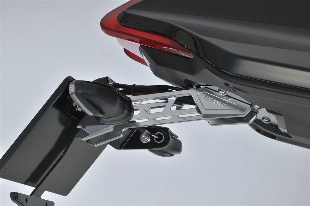■商品概要専用リフレクター付属本製品は2019年-モデル専用品となります車検対応品■詳細説明Billet license holder for。KATANA ’19---。唯一無二のスタイル。フルビレットライセンスホルダー。各車種に合わせ、最適なバランスでナンバーを保持するためにデザインし、自社にて設計・生産しています。純正の大柄かつ、長いリアフェンダーはナンバープレートや、各ライトの視認性を上げ、かつ法規に則って設計されています。その反面、サイズが過大になってしまい、せっかくの車体本体が持つデザインが生かされません。GILDdesignのライセンスホルダーは各車体に最適にマッチングし、かつ法規もクリアしています。'フェンダーを外す' ではなく。'フェンダーを魅せる'。という発想から今までにないアルミフルビレットライセンスホルダーでスタイリッシュなリアビューを演出します。純正のリアフェンダーを外し、キットを装着するだけの簡単な構造です。道路運送車両法の保安基準に適合するナンバーの角度です。アルミビレットだから実現できる構造で、十分な剛性を確保しつつ、取り付けも安易にできるように設計しました。各パーツの視認性、機能を損なわないように、ナンバー灯、ウインカー、ナンバープレートの配置にも拘りました。ただナンバープレート、補機類を保持するのを目的とせず、装着した時に車体を引き立てるようにデザイン。こだわりのアルミ削り出しブラケットにより純正のテールランプを使用できます。それにより純正の配線を加工せず複雑な配線作業をゼロにした完全ボルトオン設計です。(画像はシルバーです)。メインプレートはカウル内部への水や、ホコリの侵入を極力防ぐ形状にし、車体に取り付けた際の配線の処理も考え設計しました。連結プレートのアルマイト配色はブラックになります。デザインから設計、各部品の切削を自社にて行っています。各パーツは自社工場にて切削。材料調達、加工、表面処理など全ての工程を日本で行っています。連結プレートは10mmのアルミ板材を加工。十分な剛性を確保しつつ、軽量になるように切削します。補機類の配置、ナンバープレートの角度などを考慮し、機能美から生まれる造形美を追求した唯一無二のデザインです。【材質】A2017、A5052材使用。【表面処理】ブラックアルマイト仕上げ。【適合車種】KATANA(’19-)。2021年新保安基準ナンバー角度に対応。保安基準を満たしています。※シルバー(71547)は在庫無くなり次第廃盤です。購入ページは。こちら。です。■注意点※専用リフレクター付属 ●2021年新保安基準ナンバー角度に対応。保安基準を満たしています。※画像には他の商品が含まれている場合があります。※メーカー都合により商品の仕様変更がある場合がございます。ご了承ください。■適合車種KATANA&ensp;KATANA 年式: 19-21